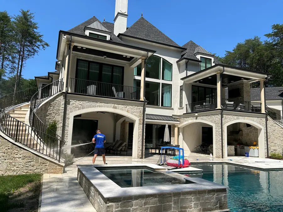 Worker pressure washing a stone pool patio surface, action shot, no before comparison.
