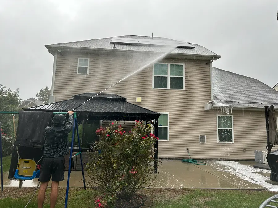 Worker soft-washing a residential asphalt shingle roof in the rain, action shot.